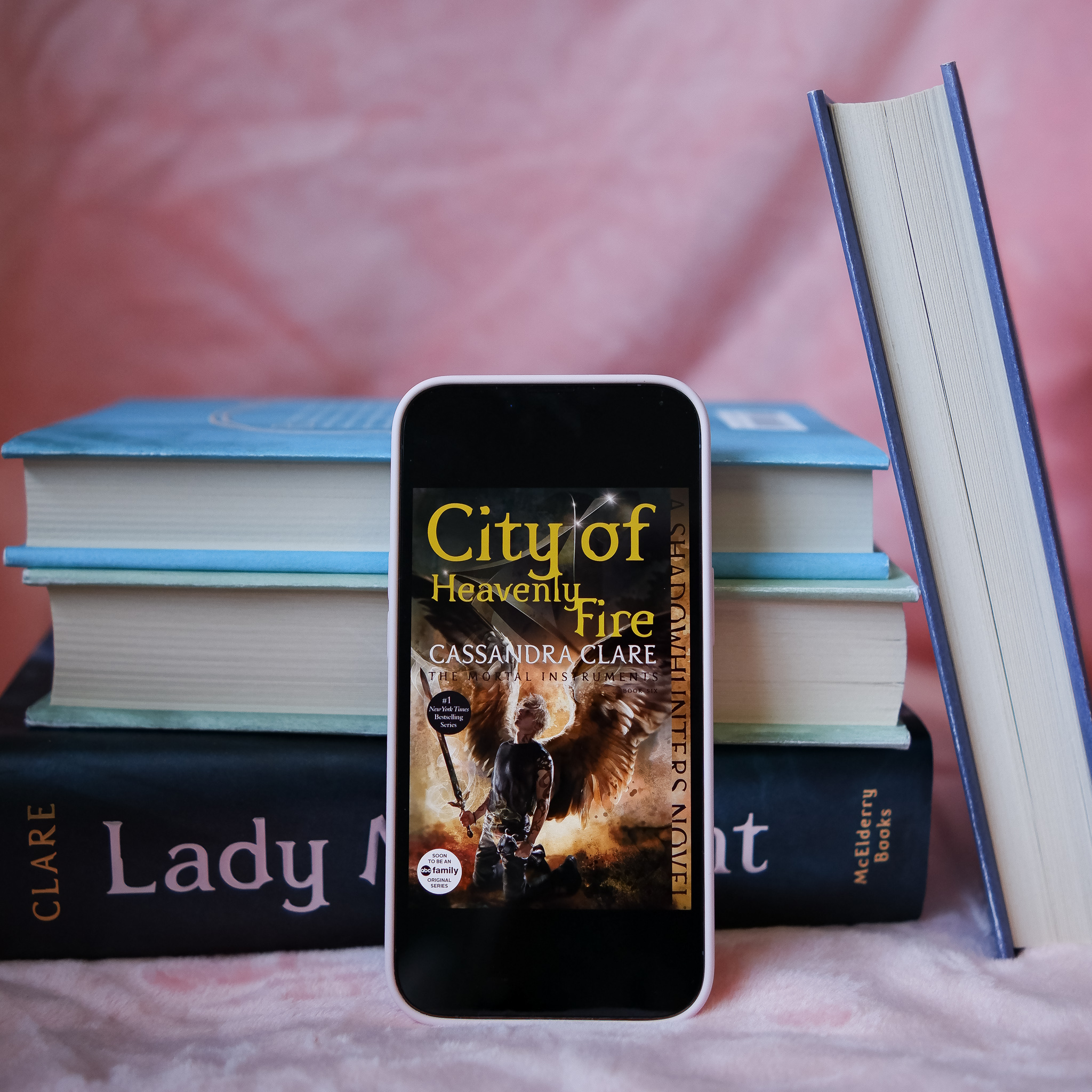 iPhone leaning up against a stack of books. The iPhone has the book cover for City of Heavenly Fire by Cassandra Clare showing on it.