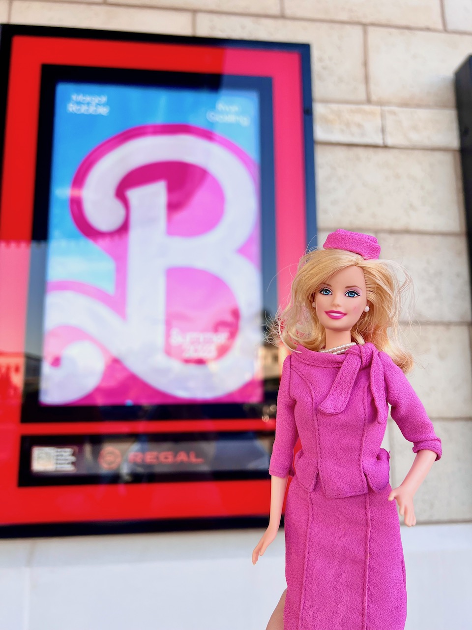 Barbie as Elle Woods from Legally Blonde 2 in the foreground, with a poster for Barbie The Movie in the background